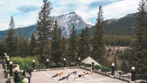 A group of people performing yoga on mats in an outdoor setting with a mountainous backdrop. - Fairmont Banff Springs Gold Experience (Banff)