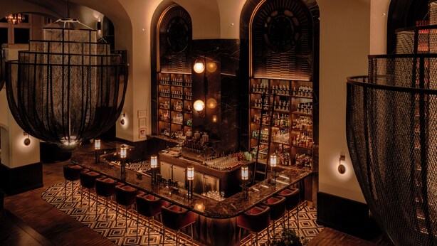 A bar area with a curved counter, bar stools, and shelves stocked with bottles. - Fairmont Banff Springs Gold Experience (Banff)