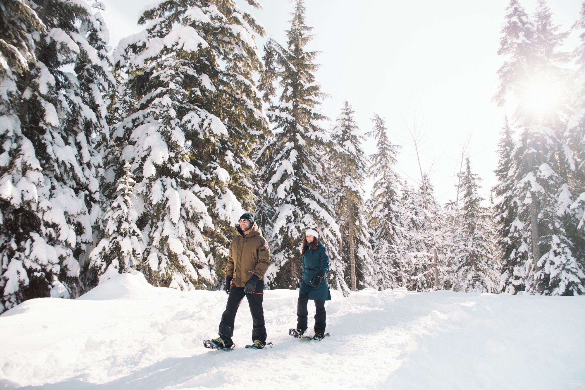Deux personnes font de la planche à neige dans une forêt enneigée.