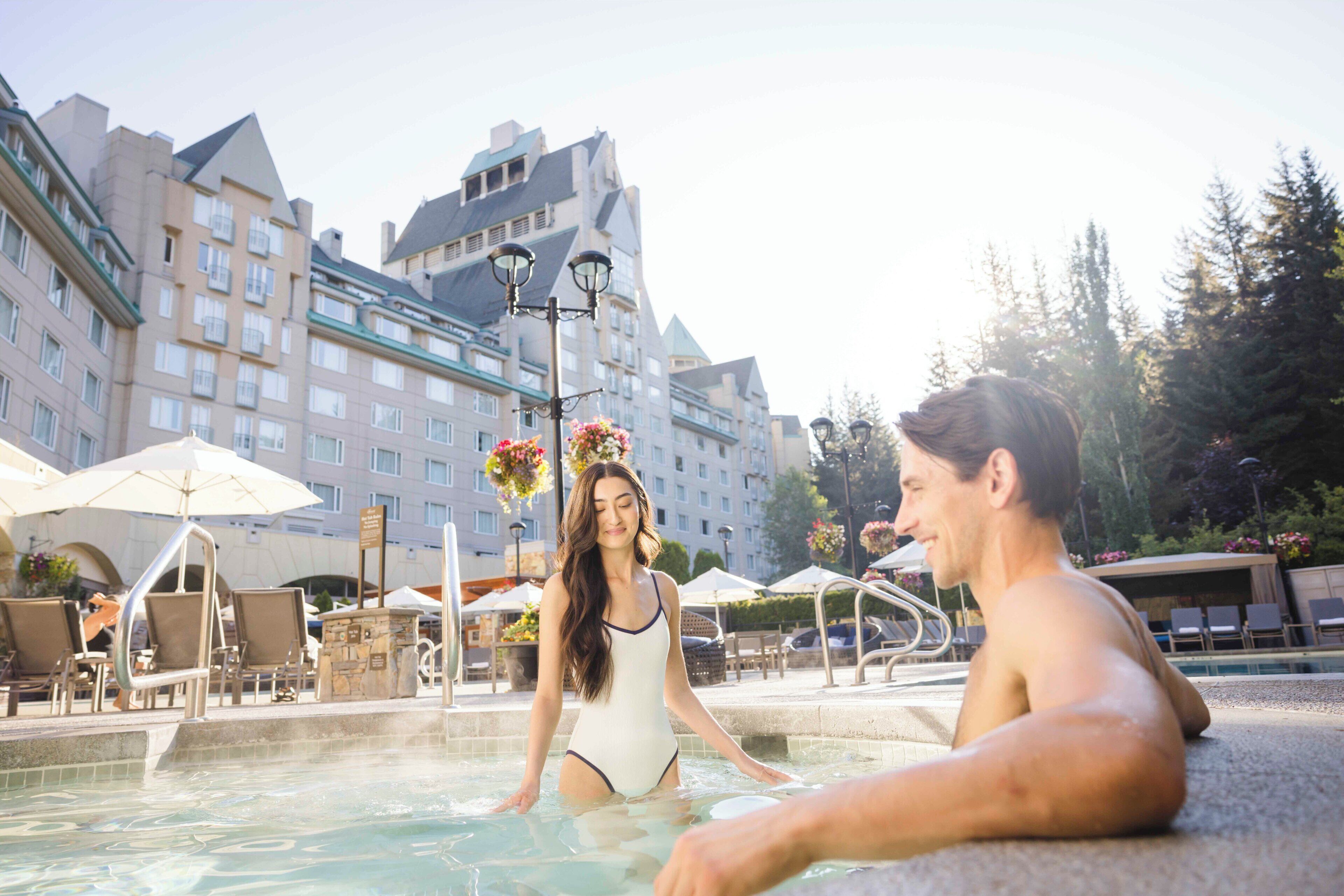 A hotel pool area with lounge chairs and umbrellas, surrounded by multi-story buildings.