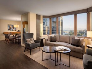 A modern hotel room with a dining area, a sofa set, a small table with a book, and large windows offering a city view. - Fairmont Chicago at Millennium Park Gold Experience (Chicago)