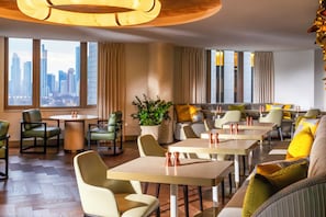 A modern dining area with tables and chairs, a potted plant, and a view of the city skyline. - Fairmont Chicago at Millennium Park Gold Experience (Chicago)