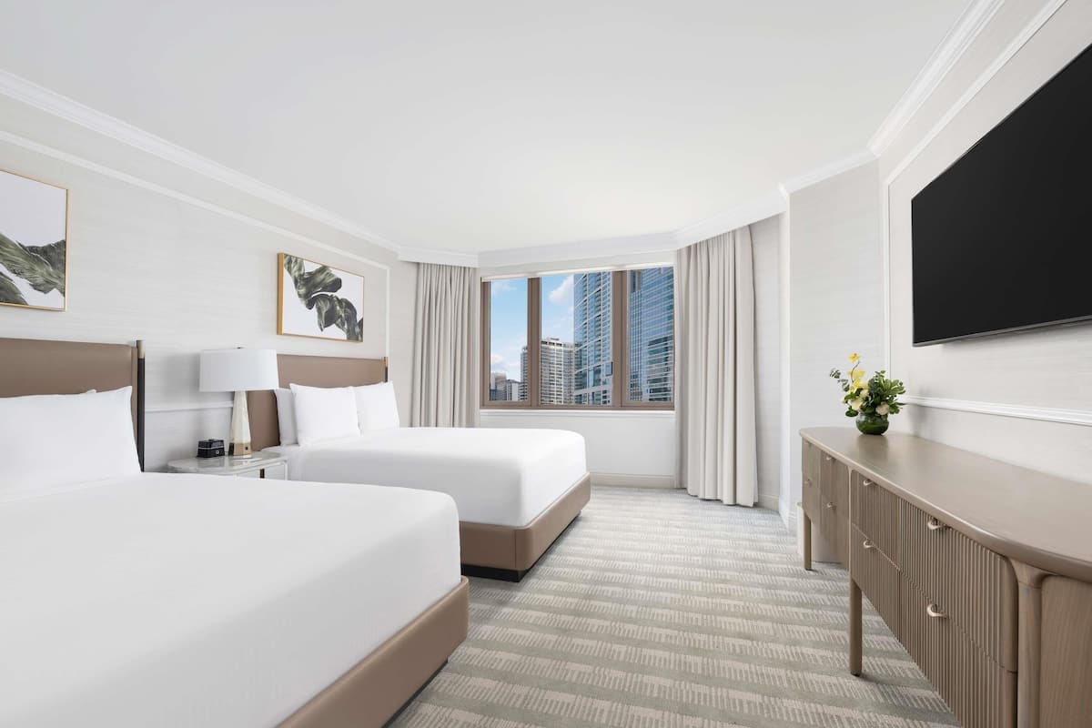 Habitación de hotel con dos camas, un escritorio, un televisor y una ventana con vistas a la ciudad.
