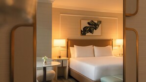 Hotellihuone, jossa on sänky, yöpöytälamput, pieni pöytä maljakolla ja seinälle ripustettu taideteos.