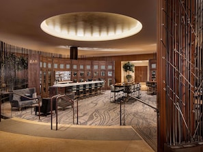 A modern bar area with a long counter, bar stools, and a decorative ceiling light. - Fairmont Chicago at Millennium Park Gold Experience (Chicago)