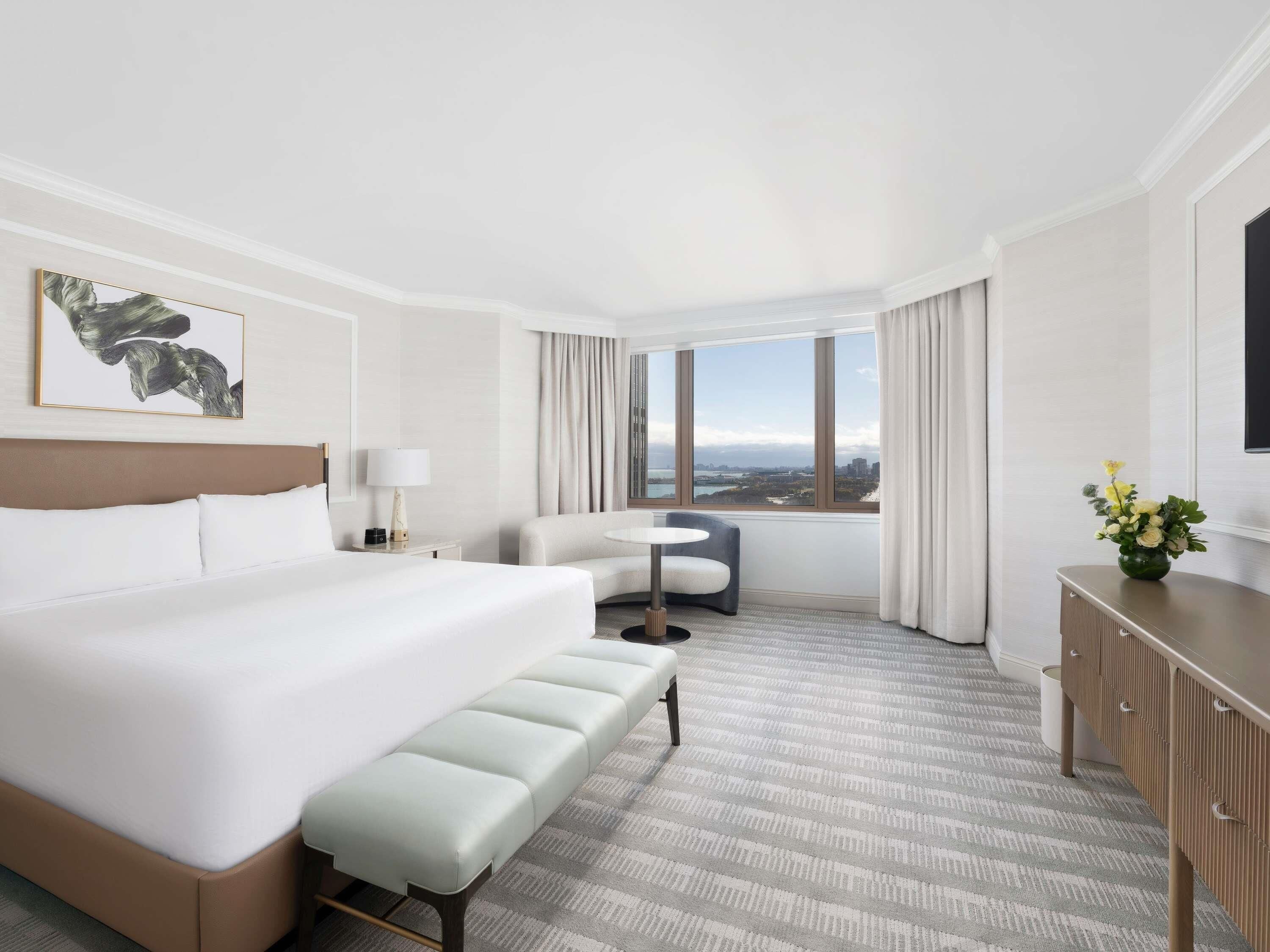 Una habitación de hotel con una cama grande, un escritorio, una silla, una mesita y vistas a la ciudad.