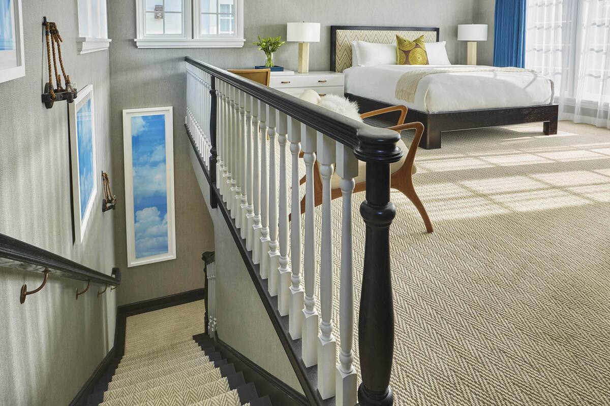 A bedroom with a bed, a nightstand, a lamp, and a view of the sky through a window.