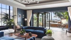 A modern living room with a blue sofa, a coffee table, and a view of the outdoors. - Fairmont Miramar Bungalows (Santa Monica)
