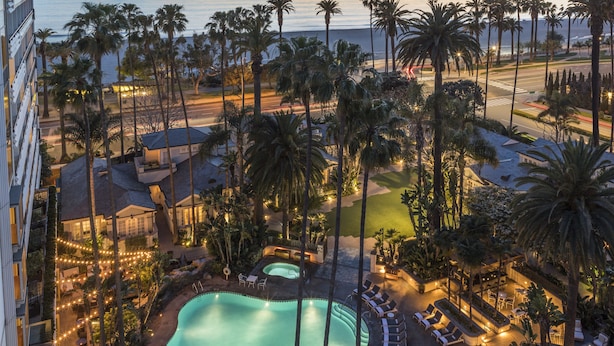 A resort with a swimming pool, lounge areas, and a view of the ocean at sunset. - Fairmont Miramar Bungalows (Santa Monica)