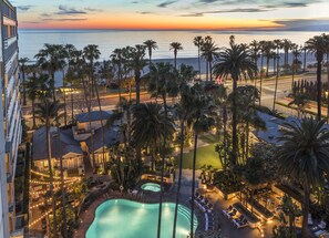 Un resort con piscina, áreas de descanso y vista al océano al atardecer.