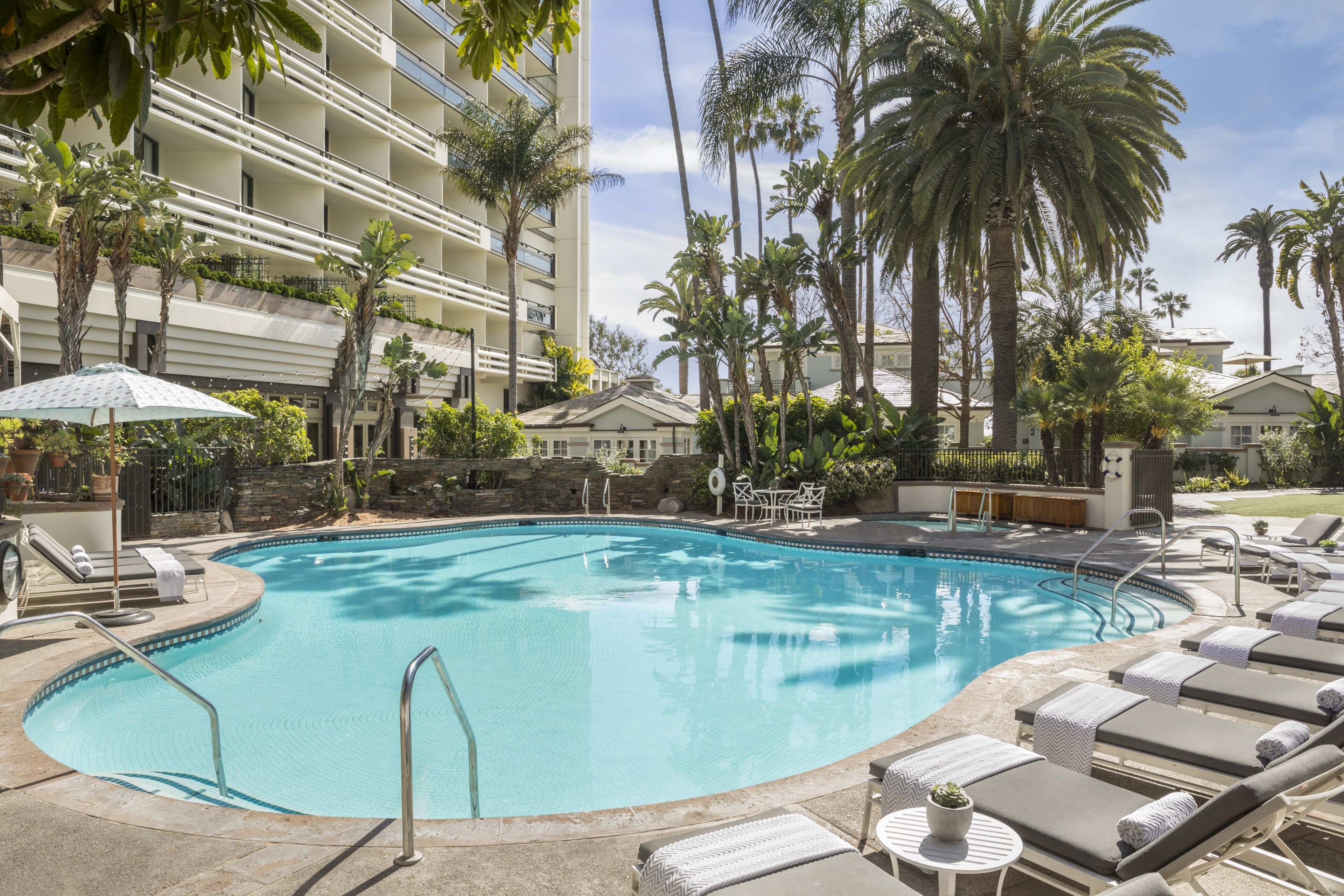 A pool area with lounge chairs, palm trees, and a building with balconies.