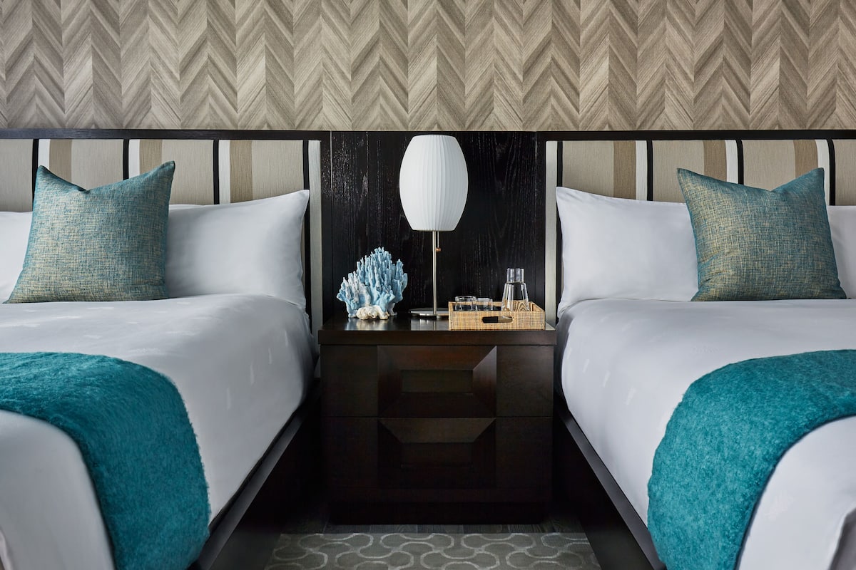 A hotel room with two beds, a nightstand, a lamp, and decorative items.