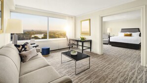 Habitación de hotel con una ventana grande, un sofá, una mesa de centro, un escritorio y una cama.