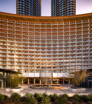 Een hoog hotel met een gelijkmatige gevel, meerdere balkons en een centrale binnenplaats met een bolvormig beeldhouwwerk.