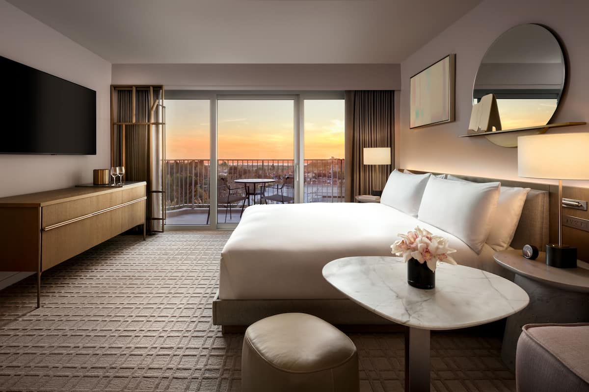 Une chambre d’hôtel moderne dotée d’un grand lit, d’une télévision à écran plat, d’une table à manger et d’un balcon offrant une vue sur la ville.
