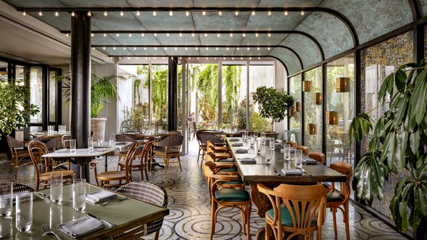 Un restaurante espacioso con techos altos, amplias ventanas y diferentes opciones de asientos, incluyendo mesas y sillas.