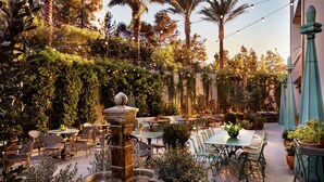 Un patio al aire libre con mesas y sillas, una fuente central y abundante vegetación.