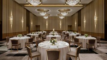 A large banquet hall with round tables, chandeliers, and wall sconces.