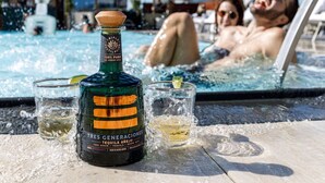 Una botella de tequila Tres Generaciones y dos vasos sobre una mesa junto a la piscina.