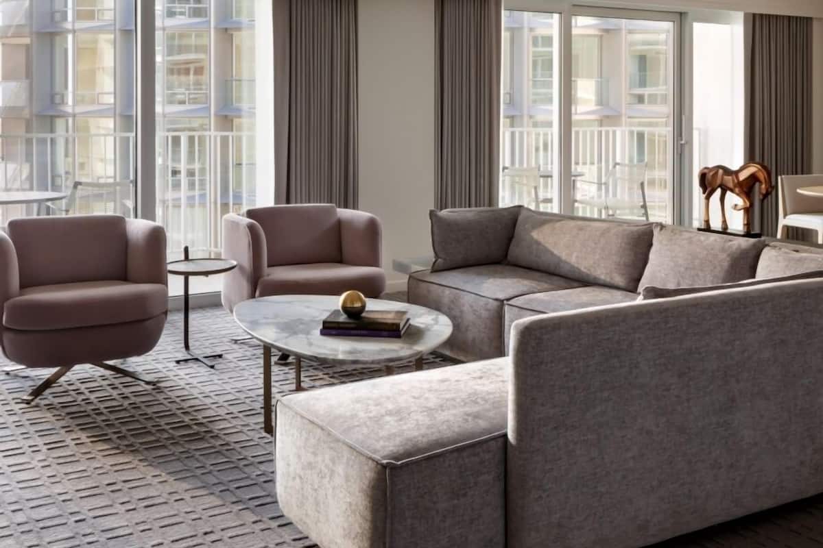 Un salon moderne avec un canapé gris, deux fauteuils, une table basse et une vue sur la ville grâce à de grandes fenêtres.