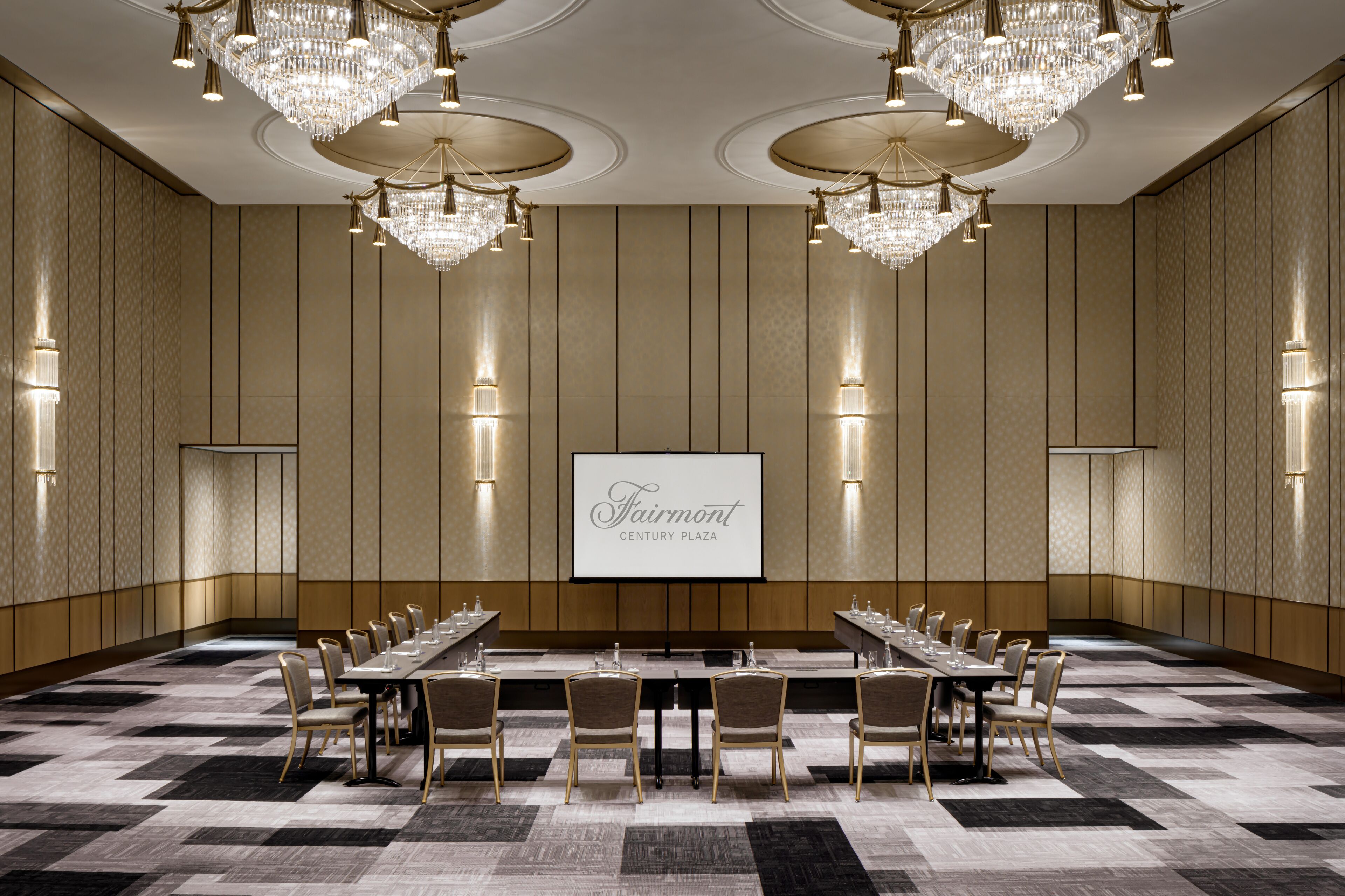 A conference room with a long table, chairs, chandeliers, and a screen displaying "Fairmont Century Plaza".