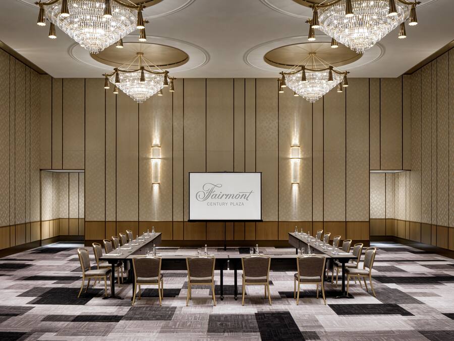 A conference room with a long table, chairs, chandeliers, and a screen displaying "Fairmont Century Plaza".