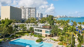 A hotel with a pool, palm trees, and a view of the ocean.