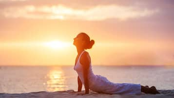 A person in a white outfit performing a yoga pose on a beach at sunset.