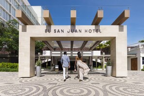 La entrada al Hotel El San Juan, con un diseño moderno, que presenta un letrero claro y un piso con diseño.