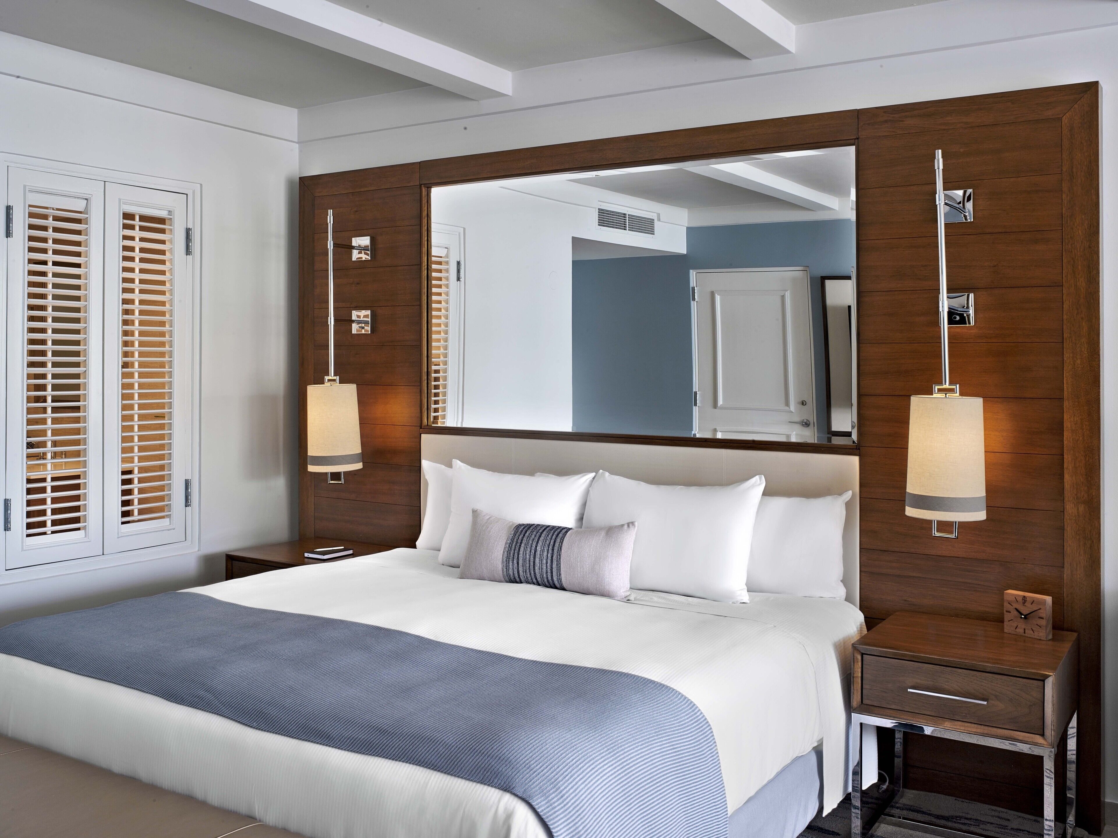 Ein modernes Hotelzimmer mit einem großen Bett, Holzpaneelen, einem großen Spiegel und zwei Nachttischlampen.