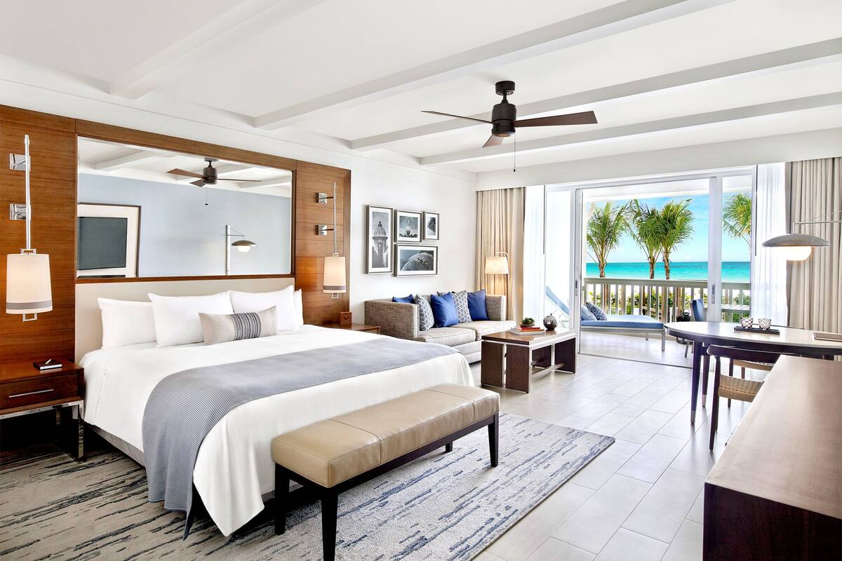 A modern hotel room with a large bed, a desk, and a balcony with a view of the ocean.
