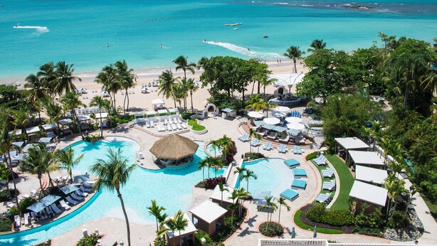 A resort with a large swimming pool, beach, and palm trees. - Fairmont El San Juan Villa Experience (Carolina)