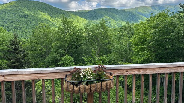Une terrasse en bois dotée d’une balustrade, qui offre une vue sur un paysage montagneux et une végétation luxuriante.