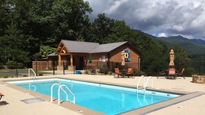 Un espace piscine agrémenté d’un bâtiment en bois, de sièges extérieurs et offrant une vue sur un paysage montagneux.