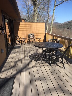 Eine Holzterrasse mit rundem Tisch und Stühlen, einer Tür sowie Blick auf Bäume und Hügel.