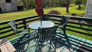 Une terrasse en bois avec une table ronde et des chaises, un banc et un parasol.