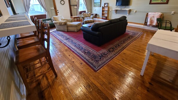 Un salon spacieux doté d’un plancher en bois, d’un canapé noir, d’un tapis à motifs rouges et d’un ventilateur de plafond.
