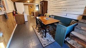 L’intérieur d’un chalet accueillant, avec une table à manger en bois, des chaises, un banc bleu et un coin cuisine.