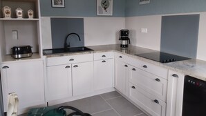 A modern kitchen with white cabinets, a black sink, a coffee maker, and a toaster. There are framed pictures on the wall and a shelf with jars. - Gite 6 people in a stone farmhouse, swimming pool, property 10Ha, panoramic view (Rocles)