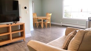 A living room with a flat-screen TV on a wooden stand, a beige sofa, and a dining area with wooden chairs and a table.