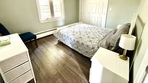 A bedroom with a bed, a desk, a chair, a window, and a door.