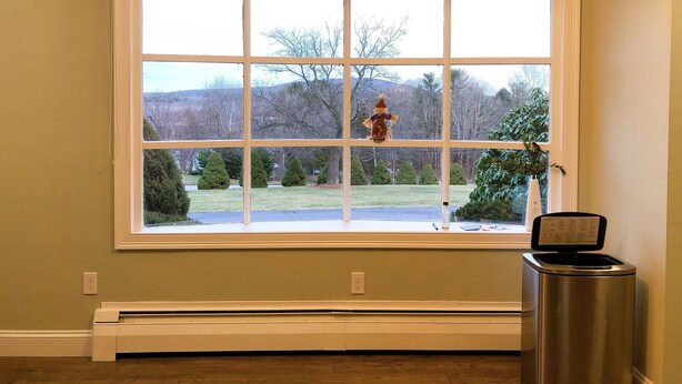 A room with a large window, a heater, and a trash can.