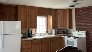Una cocina con armarios de madera, un refrigerador blanco, un microondas, una estufa y un ventanal.