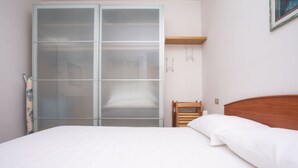 Ein Schlafzimmer mit einem Bett, einem Holz-Kopfteil, einem Kleiderschrank mit Milchglasschränken und einem kleinen Holzstuhl.