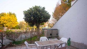 Eine Terrasse im Freien mit Tisch und Stühlen, umgeben von einer weißen Mauer und einem Baum.