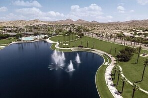 A large lake with fountains, surrounded by a well-maintained lawn and palm trees, with mountains in the background. - 🏖️ Endless Summer Retreat | Private Pool & Goodyear Spring Training (Goodyear)