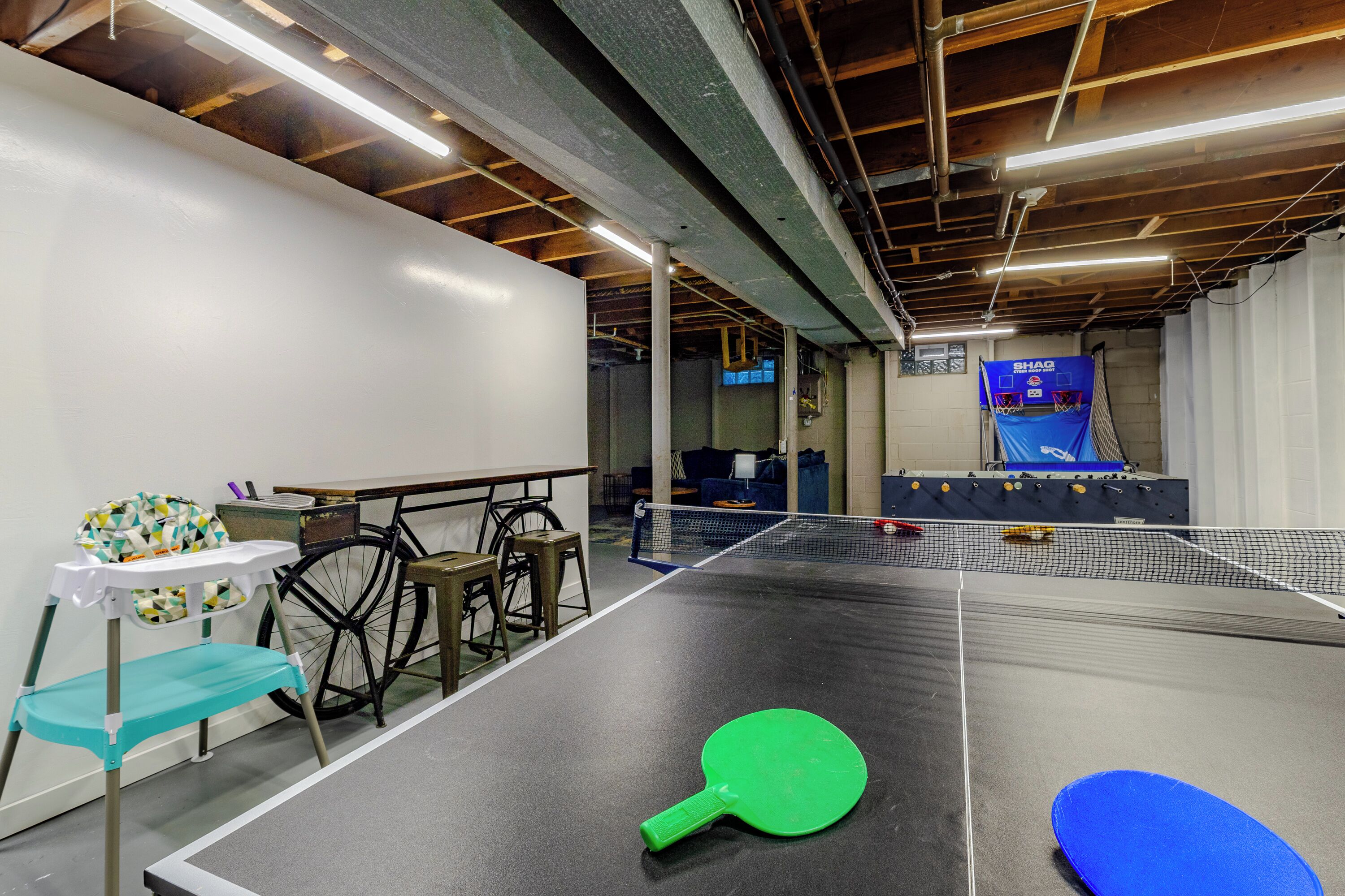 Una mesa de ping pong interior con una red, una paleta verde y una paleta azul sobre la mesa.