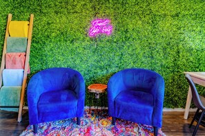 Una habitación con dos sillones azules, una mesita de madera y un letrero de neón que dice 'Treat Yo' Self'.