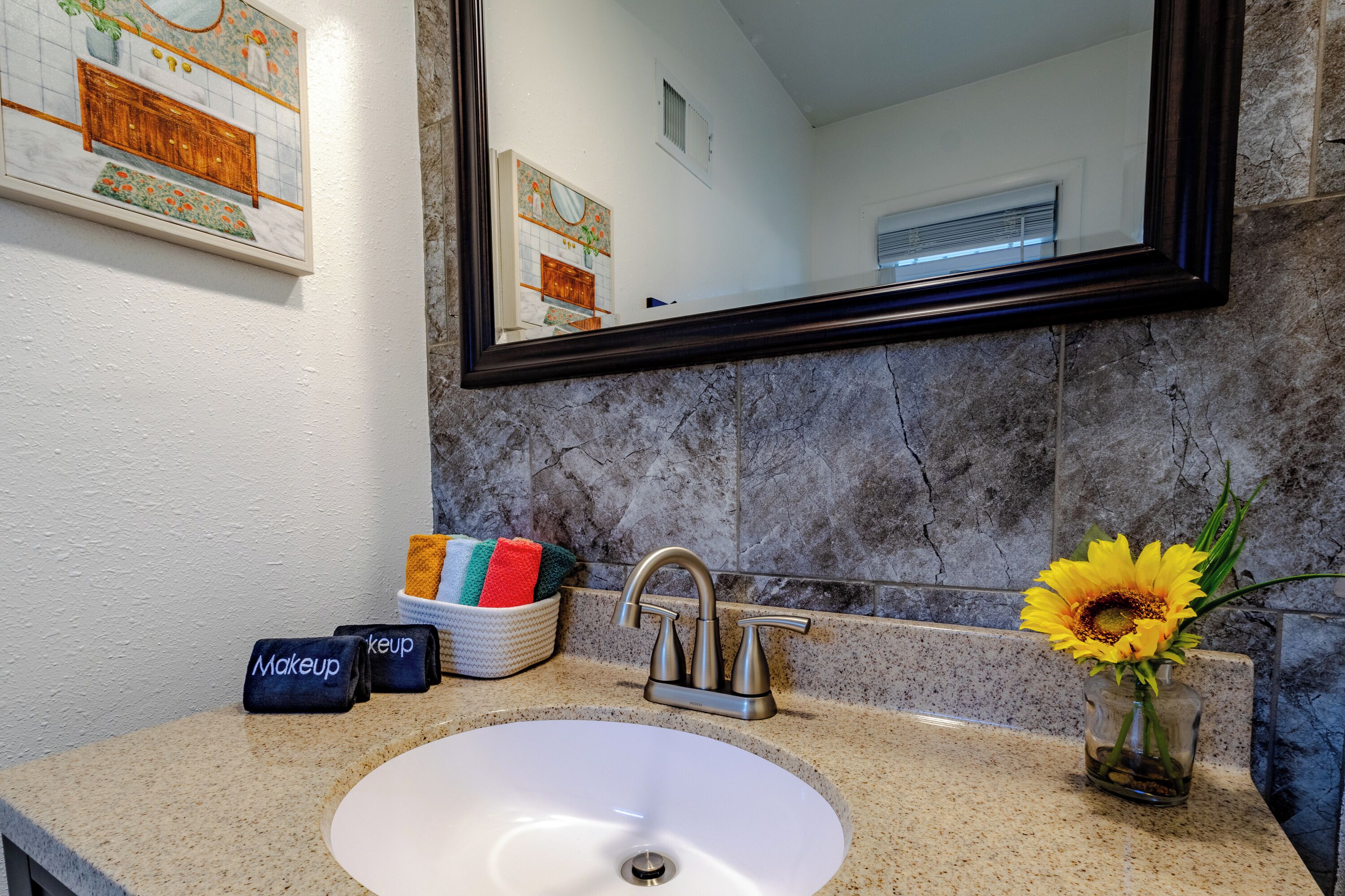 A bathroom with a white sink, a mirror, and a vase with a sunflower.