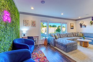 Una sala de estar moderna con una pared verde, un letrero de neón, un sofá modular, un sillón azul y una mesa de centro.